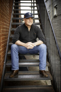 Promotional photo of Ace Atkins sitting on stair case wearing a baseball cap